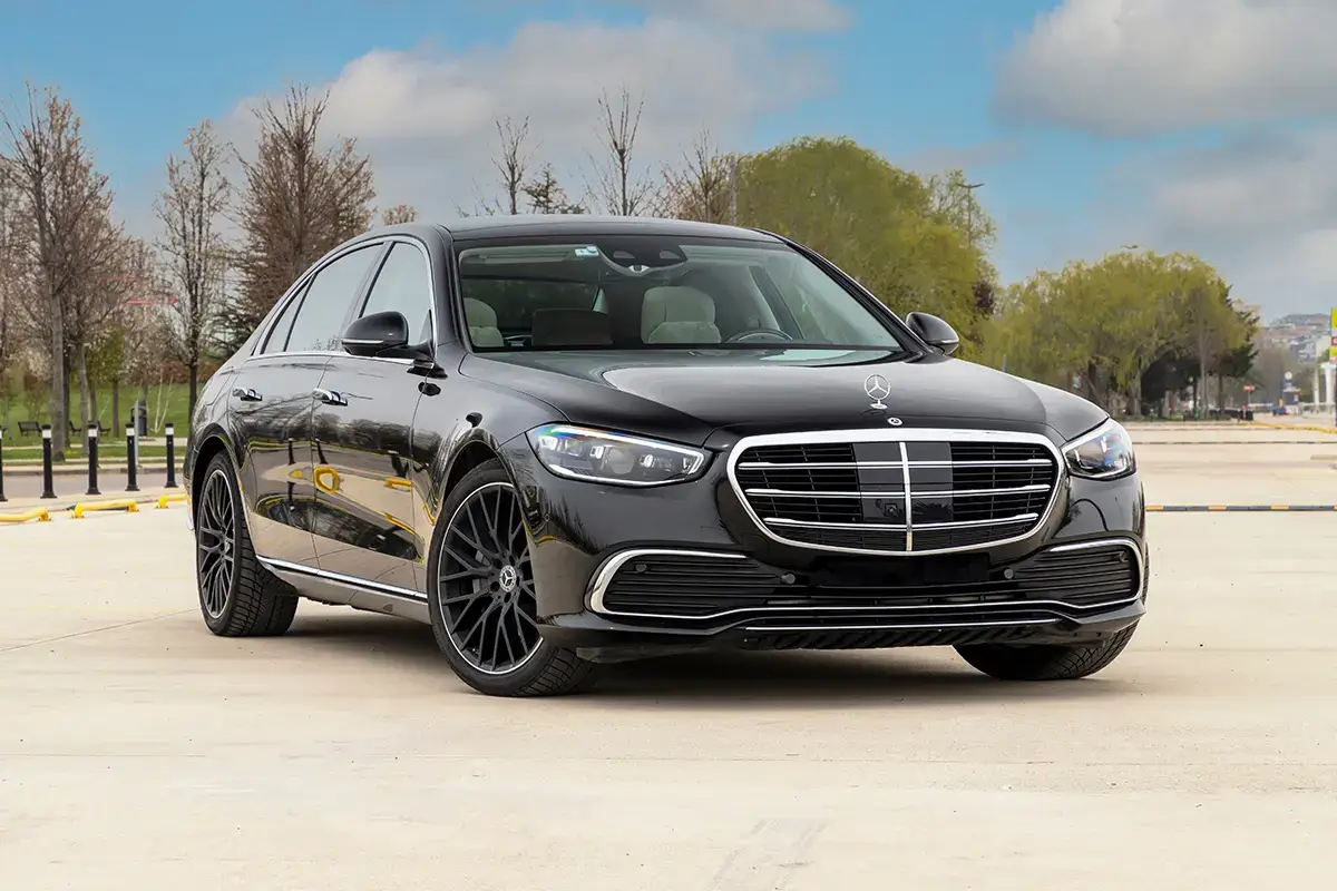 Mercedes-Benz Classe S noire haut de gamme, cadrée de trois-quarts avant sur un parking dégagé.